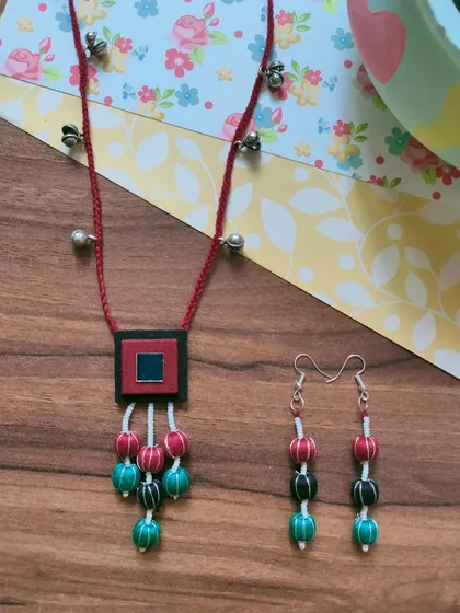 This necklace set features a fabric pendant with colorful thread-wrapped beads. The matching long earrings complete the look, making it an easy choice for Durga Puja or Navratri celebrations.