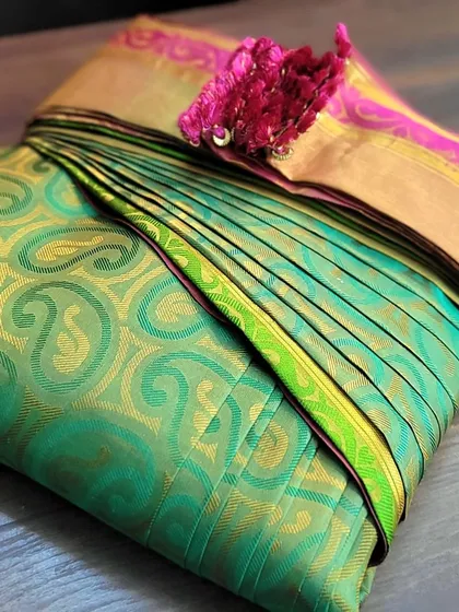 A client's green Kanjivaram saree with a bright pink pallu, perfectly folded.