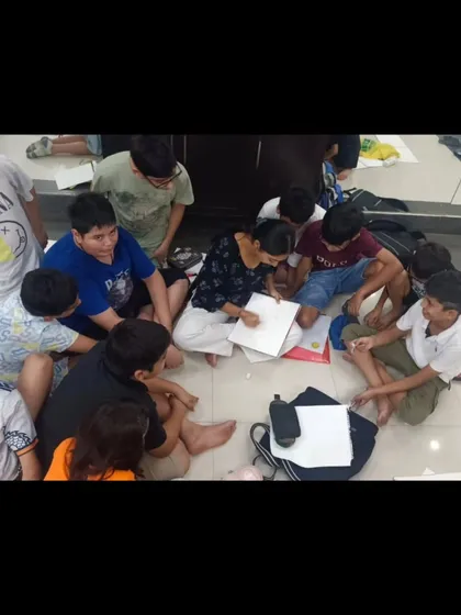 An instructor sits on the floor with a group of students, providing hands-on guidance for a drawing project. This collaborative and informal setting encourages open communication and learning.