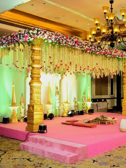 This South Indian style mandap features magnificent golden temple pillars and a canopy of hanging floral strings. The design is both grand and traditional, set on a vibrant pink stage for a stunning visual contrast.