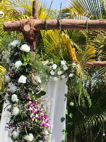 The top of the rustic wooden mandap, where the crossbeam is tied with jute rope and decorated with cascading floral arrangements, blending seamlessly with the surrounding nature.