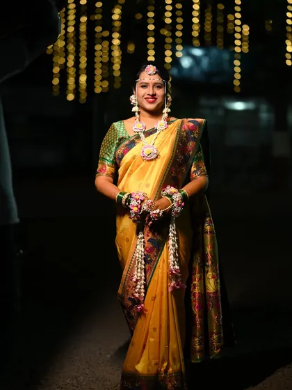 The bride stands radiant and ready for her Haldi ceremony. Her full floral jewellery set, including the long necklace and hathphool with kalire, creates a stunning silhouette.