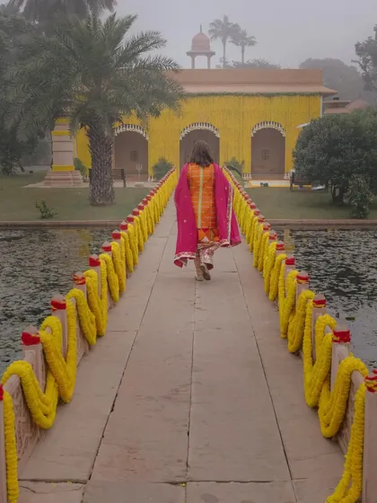 The bride's mother walks across a marigold-lined bridge to the temple to prepare for the haldi ceremony. This quiet, solitary moment of preparation is a beautiful part of the wedding story.