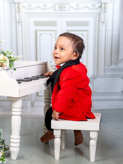 A little maestro in a striking red jacket. He's ready to play a masterpiece on the miniature piano in our elegant studio setting.