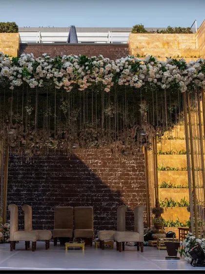 A grand mandap setup at the Grand Hyatt Mumbai, featuring a stunning overhead floral installation against a dramatic stone wall.