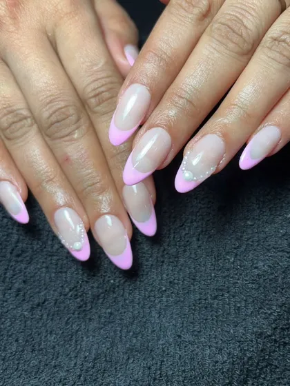 A soft and pretty French manicure with pastel pink tips on almond-shaped nails. Tiny pearl accents at the cuticle add a touch of simple elegance.