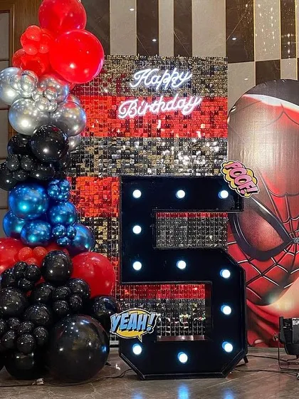 A close-up of the Spider-Man setup, showing the large light-up number '5', a silver sequin wall, and a giant inflatable Spider-Man head.