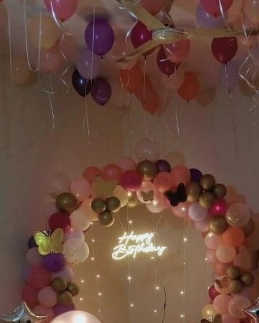 A cozy birthday setup with a multi-colored balloon arch, fairy lights, and butterfly accents.