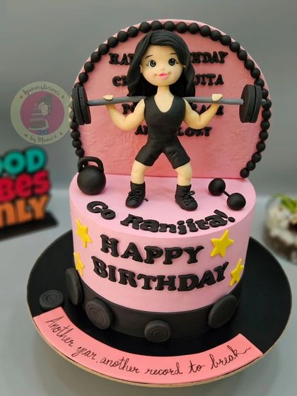 A cake for a professional weightlifter, featuring a strong female figurine and gym equipment.