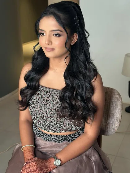 A seated portrait showing off the full look. The glam makeup is paired with voluminous waves in a high ponytail for a chic, modern vibe.