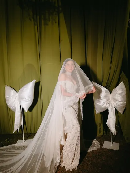 The bride, a vision in her veiled gown, standing beside oversized satin bows that were a signature element of her reception decor.