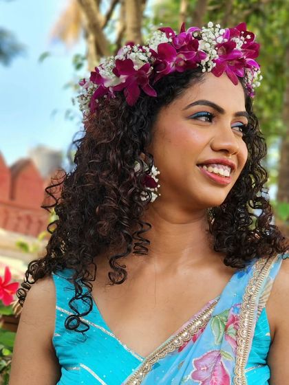 A Hawaiian princess look for a Haldi ceremony. The bride's natural curls are adorned with a beautiful crown of fresh orchids, creating a unique and stunning style.
