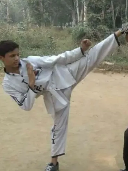A student executing a perfect high kick during outdoor training. This demonstrates a combination of flexibility, balance, and power.