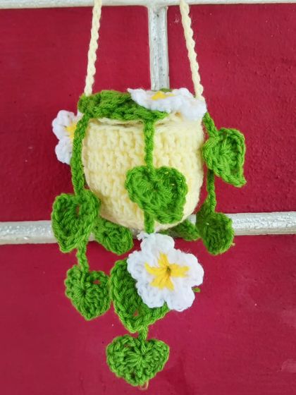 A hanging pot of crochet flowers, designed to be used as a car mirror charm or a small wall hanging.