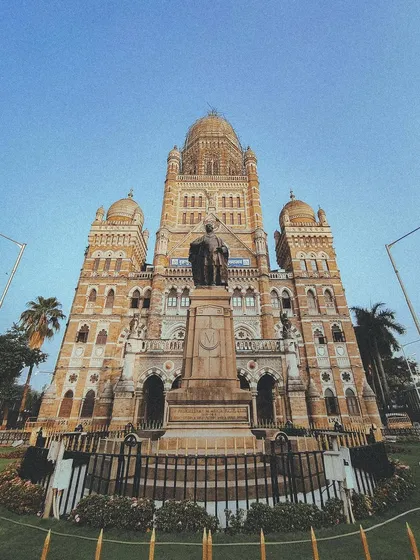 The grand statue of Sir Pherozeshah Mehta stands before the impressive BMC headquarters. A low-angle shot that emphasizes its scale and importance.