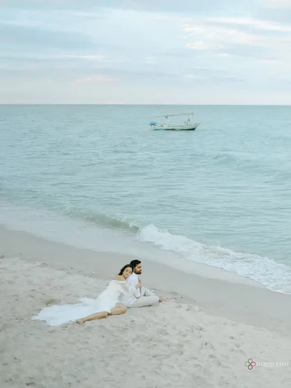 A wide shot of the couple relaxing on a pristine beach in Thailand, with a lone boat on the tranquil sea. This image evokes a feeling of peace and seclusion.