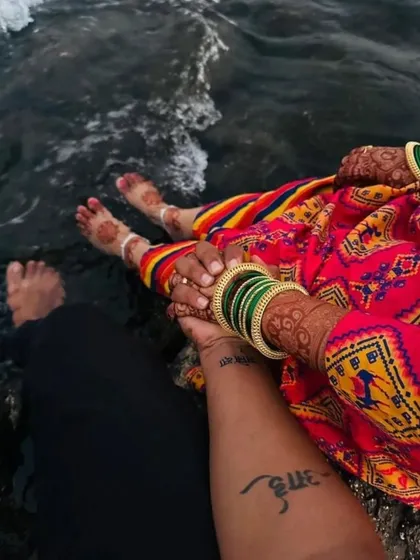 An artistic shot of a couple by the water, highlighting the bride's beautiful foot mehndi. The simple mandala design is elegant and looks stunning against the natural backdrop.