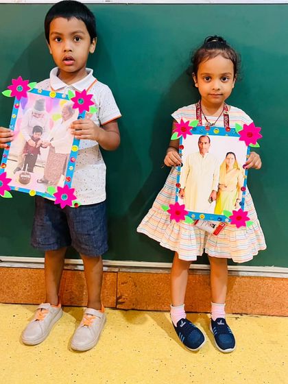 Two children hold up their handmade photo frames, a heartfelt gift for their grandparents. These simple gestures help strengthen family bonds.
