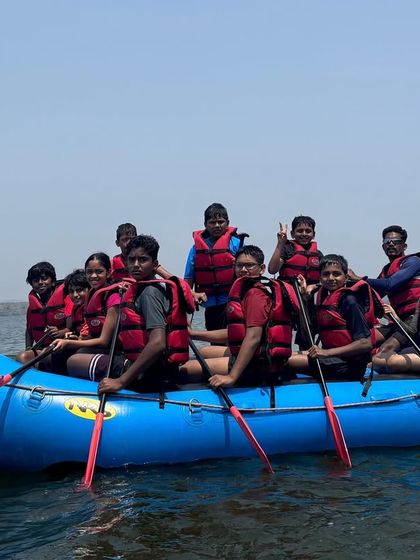A full raft of smiling campers paddles together during a session at Vani Vilas Sagara.