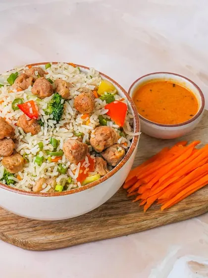 A nutritious soya chunk and vegetable rice bowl, presented on a wooden board with a dipping sauce and fresh carrots. The clean styling is perfect for showcasing healthy meal options on delivery apps.