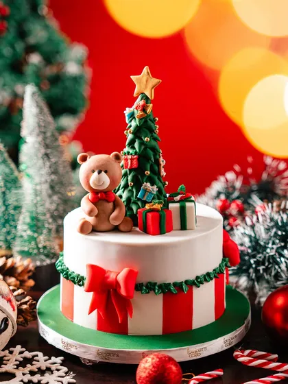 A custom two-tiered Christmas cake, featuring red and white stripes on the bottom tier and a charming scene on top with a fondant teddy bear and Christmas tree. It's a storybook cake for a magical celebration.