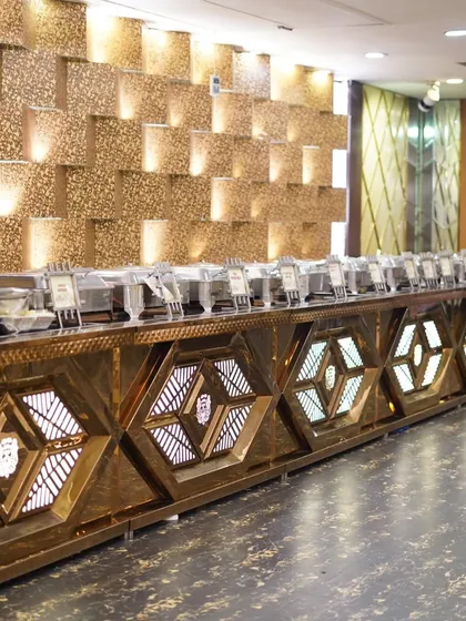 The lavish catering setup at a wedding reception. The golden, geometric patterns of the buffet counter add to the luxurious feel.