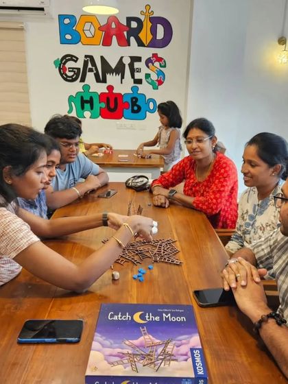 Patrons enjoying games at the Board Games Hub, with my custom-designed logo mural in the background.