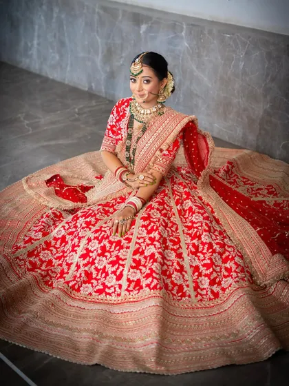 A magnificent wide shot showcasing the grandeur of the bride's lehenga. The makeup is kept soft and radiant to balance the opulence of her attire, creating a look of pure grace.