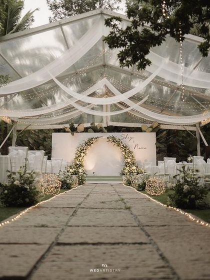 A breathtaking view of a wedding reception under a clear-top tent. The fairy lights along the aisle and the elegant white decor create a truly magical scene.