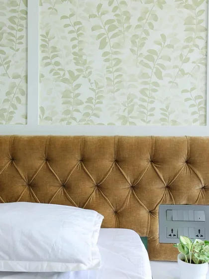 A close-up of the tufted mustard headboard, whose rich texture and color contrasts beautifully with the delicate wallpaper.