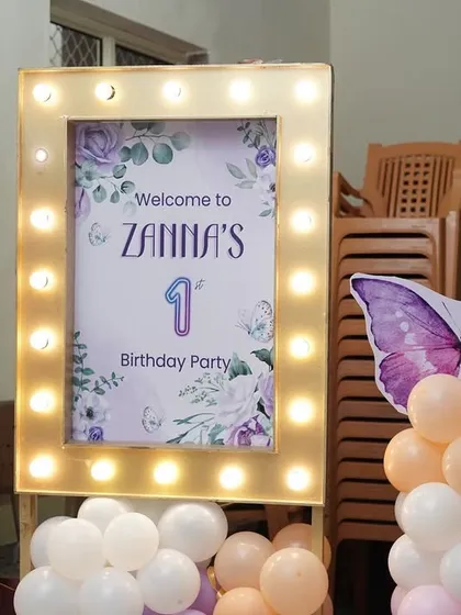 The lit-up welcome sign for Zanna's butterfly-themed celebration, flanked by pastel balloon columns.