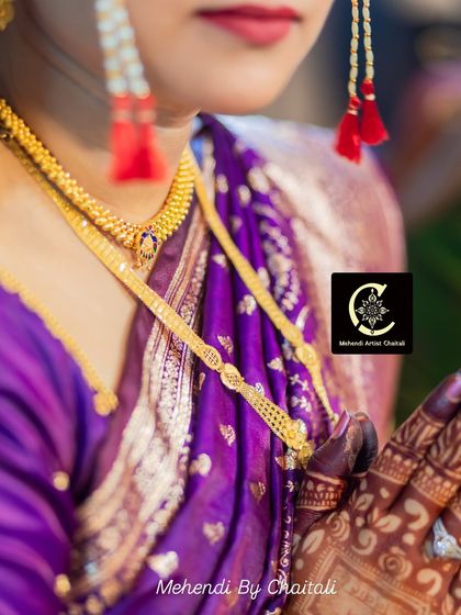 A close up of the bride's hands, showcasing the stunning contrast between the dark mehendi stain and her traditional gold jewelry and purple saree.