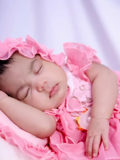 A one-month-old baby girl sleeping peacefully in a beautiful pink dress and bonnet. We have a variety of outfits for your baby's session.