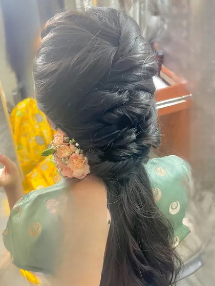 An intricate and voluminous braided ponytail with a floral accessory.