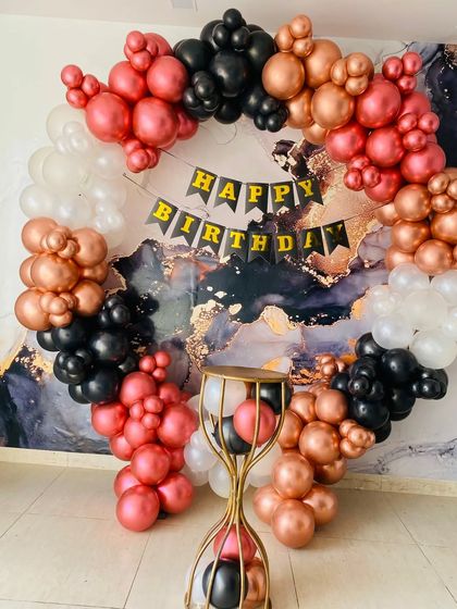A dramatic balloon ring against a marble-patterned backdrop. The mix of metallic rose gold, red, and black balloons makes for a very sophisticated and bold statement.