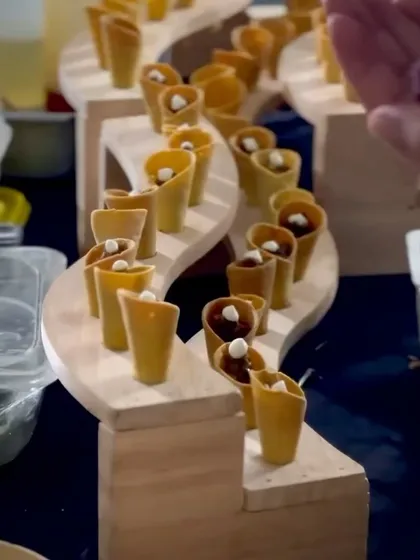 A winding, multi-level wooden stand displays a series of edible chaat cones. This unique serving method adds architectural beauty to the food presentation.