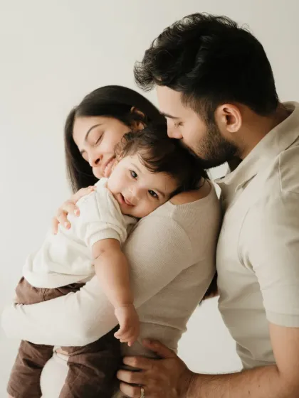 A tender moment between parents and their baby. The baby rests on mom's shoulder while dad leans in, creating a feeling of safety and love.