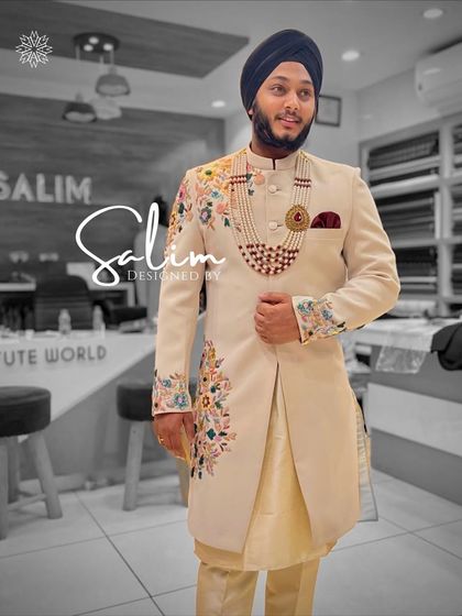 A groom in a light cream sherwani featuring colorful floral embroidery on the shoulder and cuff. The look is accessorized with a multi-layered necklace, adding a touch of modern elegance.