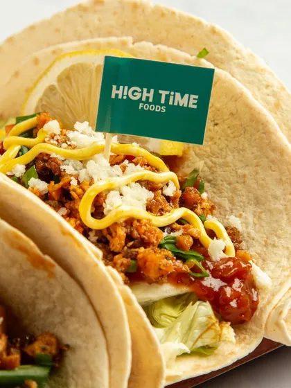 A close-up of a plant-based meat taco, with a branded flag. The focus is on the texture of the filling and the fresh toppings, making it look like a delicious and healthy fast-food alternative.