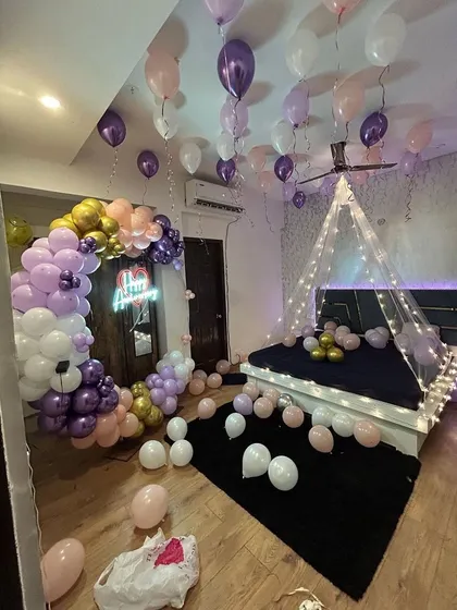 A dreamy bedroom decoration with a pastel balloon arch and a fairy light canopy over the bed. The purple and pink balloons create a soft and magical atmosphere.