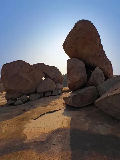 The sun backlights a formation of giant boulders, creating strong silhouettes and shadows. This shot highlights the dramatic and almost otherworldly geology of the area.