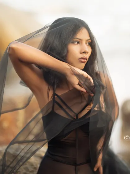A close-up portrait with the model's face partially veiled by the sheer black fabric. This creates a sense of mystery and adds an artistic touch to the beach shoot.