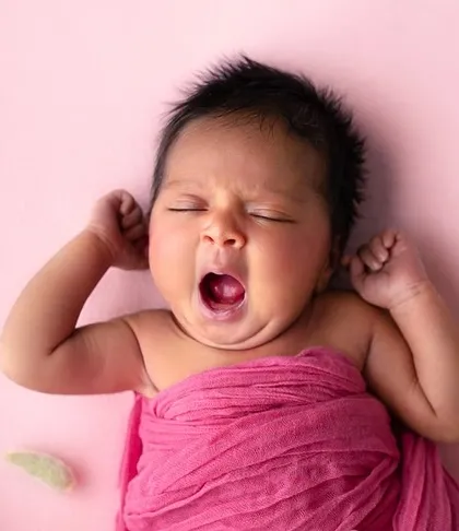 A big yawn from a newborn wrapped in a hot pink swaddle. These candid, unposed moments are often the most cherished memories.