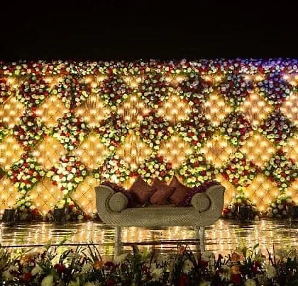 A truly grand wedding stage I created, featuring a massive wall of fresh flowers arranged in a diamond pattern with integrated lighting. This kind of opulent backdrop makes for stunning photographs and leaves a lasting impression on guests.