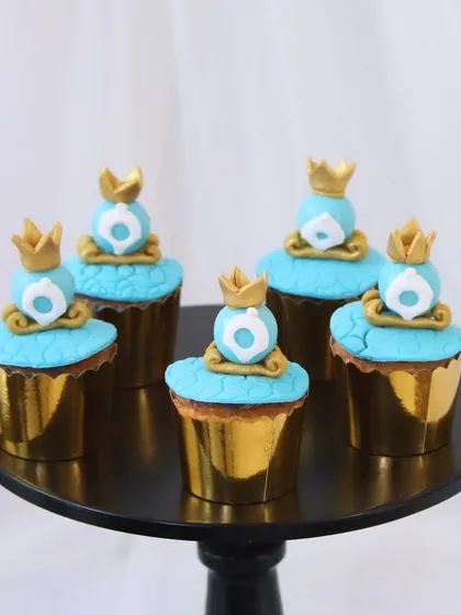 These Cinderella-themed cupcakes are perfect for a fairytale birthday party. Each one is topped with intricate, handcrafted fondant details, including delicate blue frosting and edible gold crowns, all presented in elegant gold foil liners.