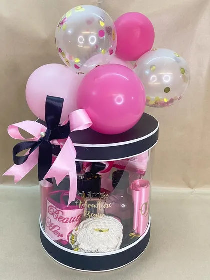 A 'Bride To Be' hamper from her bride tribe. This clear cylindrical box is filled with pink and black themed goodies and topped with a balloon bouquet.