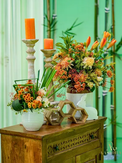 A rustic console table with an arrangement of orange lilies and chrysanthemums, paired with wooden honeycomb decor and pillar candles.
