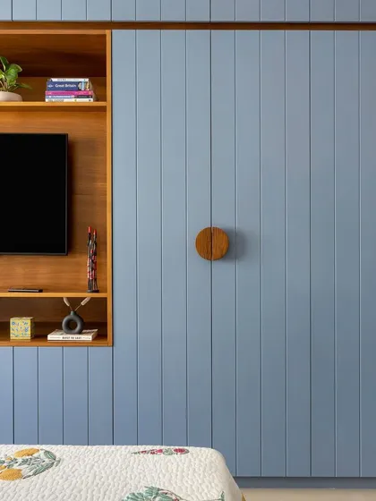 This bedroom features a floor-to-ceiling wardrobe with fluted panels finished in a calming blue. An integrated TV niche and custom circular wooden handles make it a functional focal point.