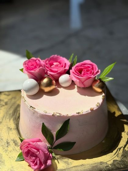 A simple and sweet pink cake decorated with fresh pink roses and gold and white spheres. The gold leaf accents add a touch of elegance to this lovely design.