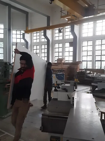A student carries a large, pre-laminated board to the CNC machine, ready for cutting. Our training covers the entire workflow, from material handling to final product.